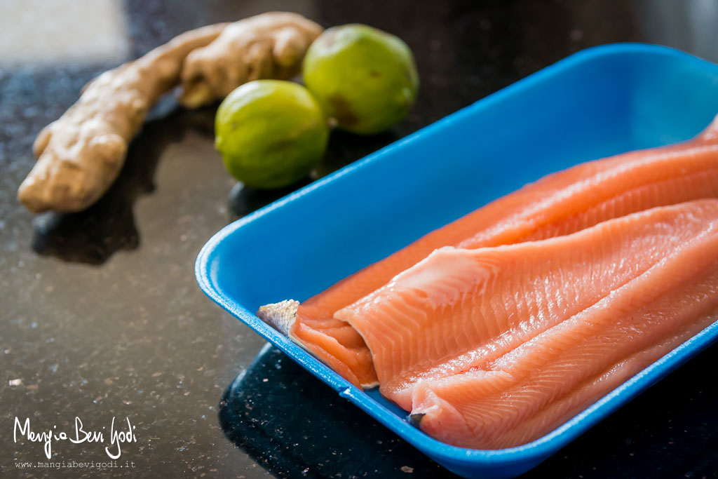 Vaschetta con filetti di trota salmonata e sullo sfondo una radice di zenzero e 2 lime