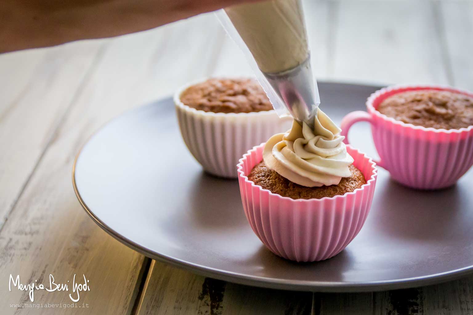Decorare i cupcakes alla nutella con il frosting al caffè applicandolo con una tasca da pasticcere.