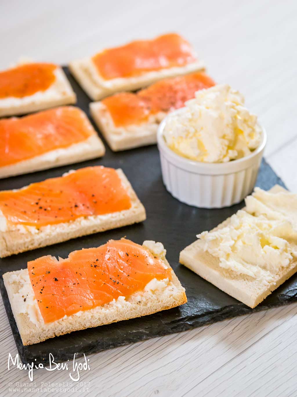 Crostini con salmone serviti su piatto di ardesia insieme a una ciotola di burro montato 