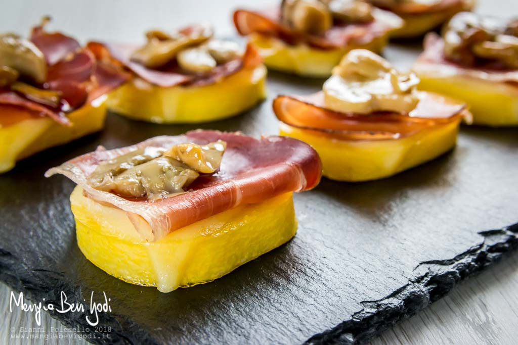 Antipasto di polenta, speck, provola e funghi sopra piatto di ardesia