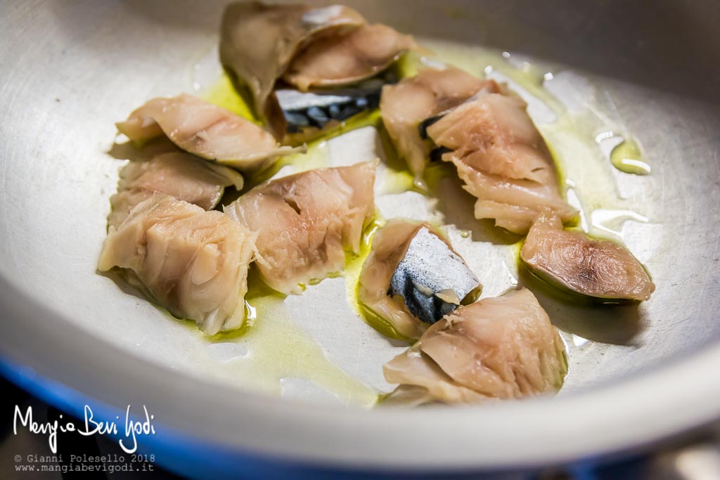 Cottura di sgombro tagliato a pezzi in padella di alluminio con poco olio extravergine di oliva