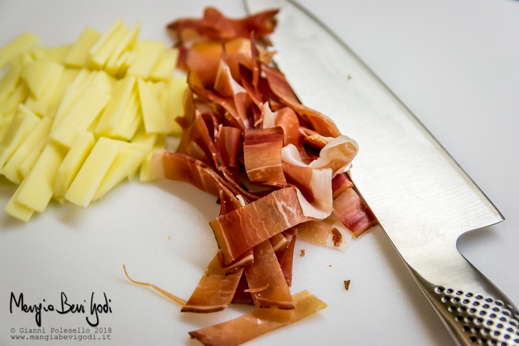 Speck e provola tagliati a fette su tagliere bianco con coltello di acciaio