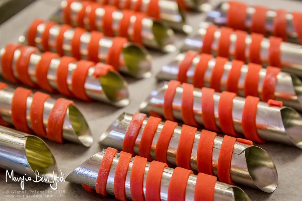 Stelle filanti rosse arrotolate intorno a cilindri per cannoli imburrati e disposte sopra una teglia coperta da carta da forno