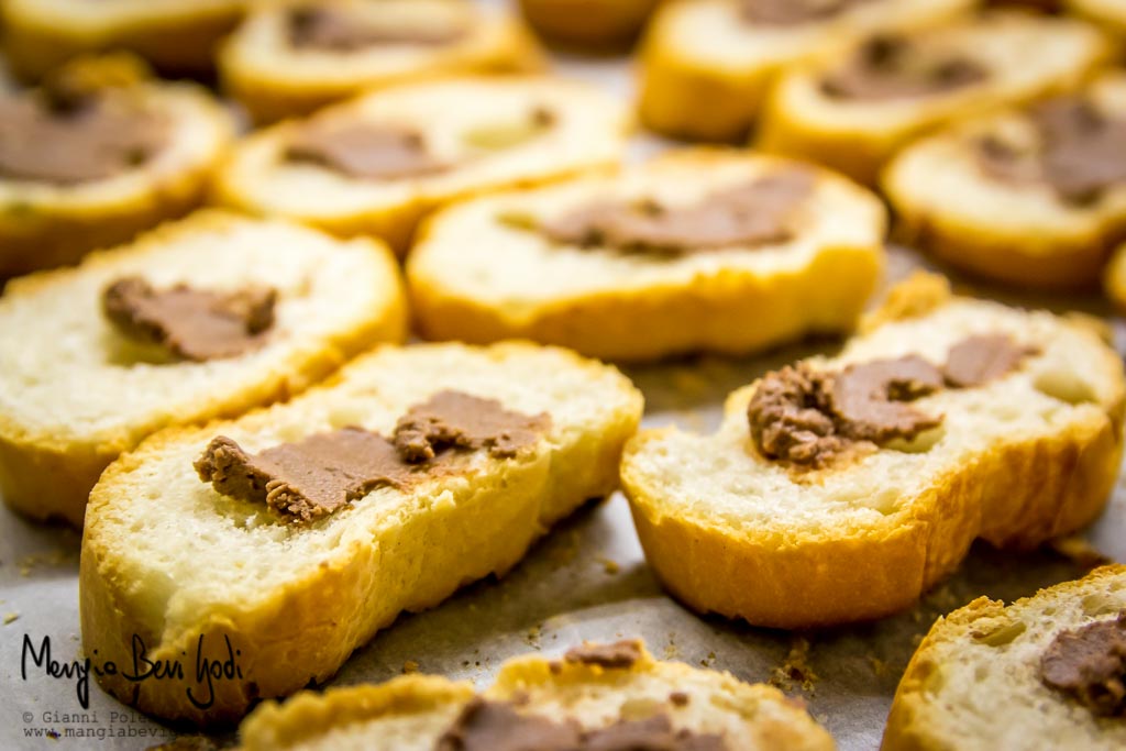 Fette di baguette tostate spalmate di pasta d'acciughe disposti su placca da forno