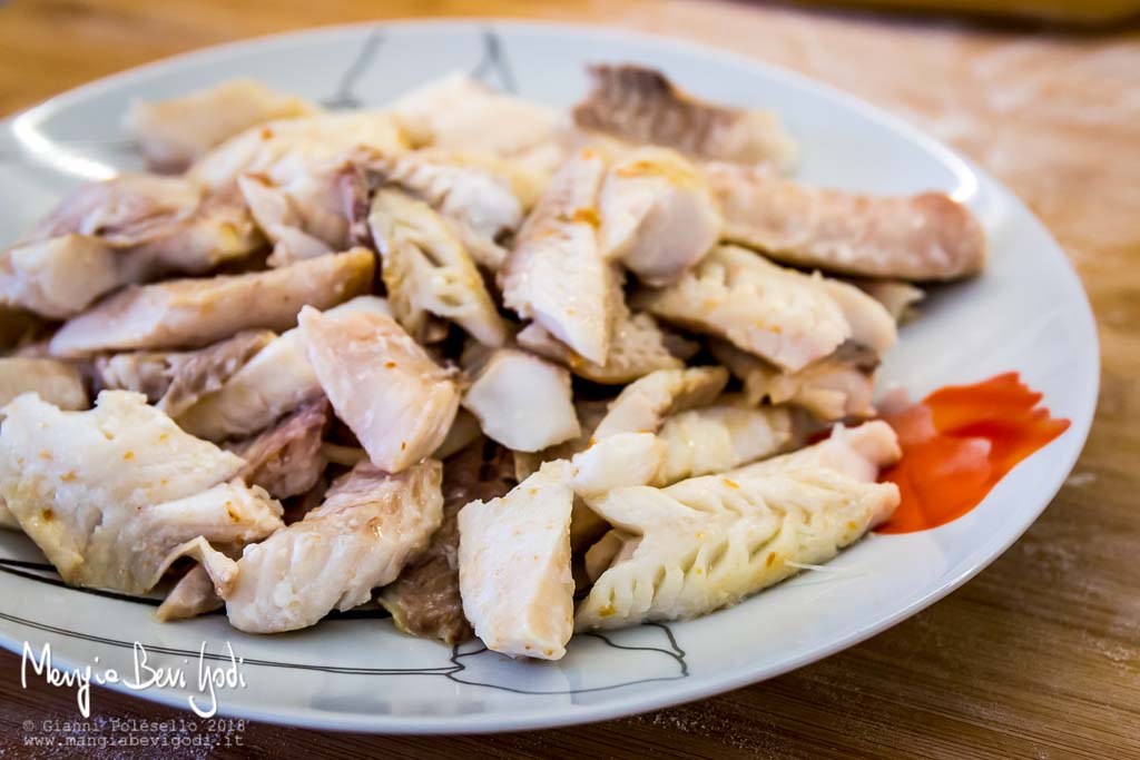 Rimozione lische da filetti di scorfano cotti su piatto bianco.