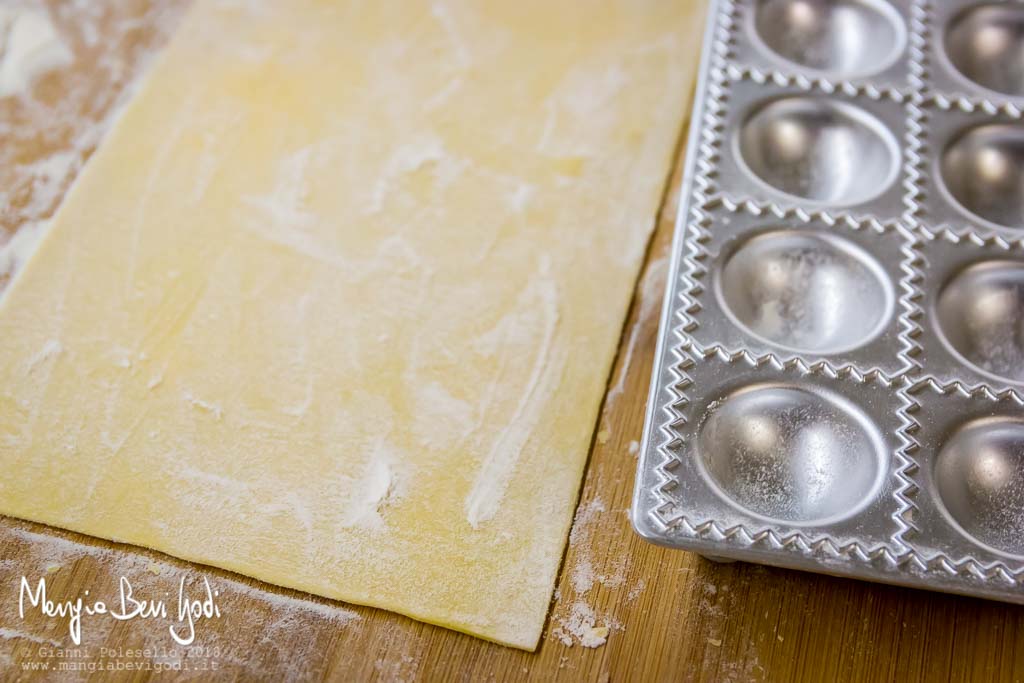 Stampo per agnolotti e sfoglia di pasta fresca su tagliere di legno infarinato