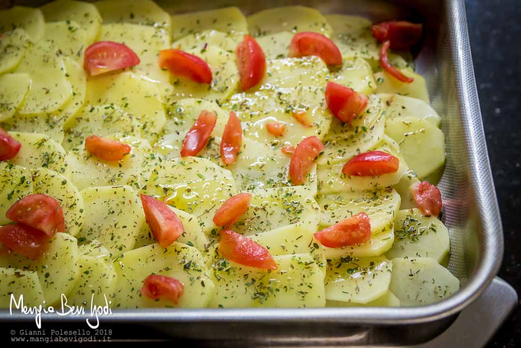 Teglia da forno ricoperta con un letto di patate e pomodorini