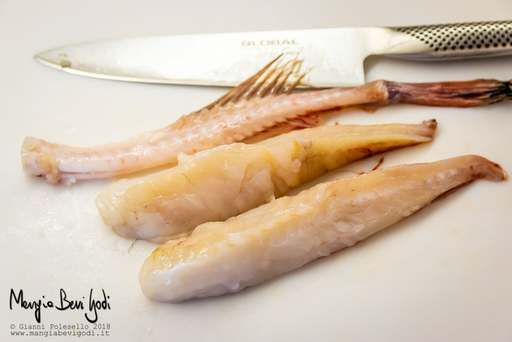 Filetti di rana pescatrice, lisca centrale e coltello posati su tagliere bianco