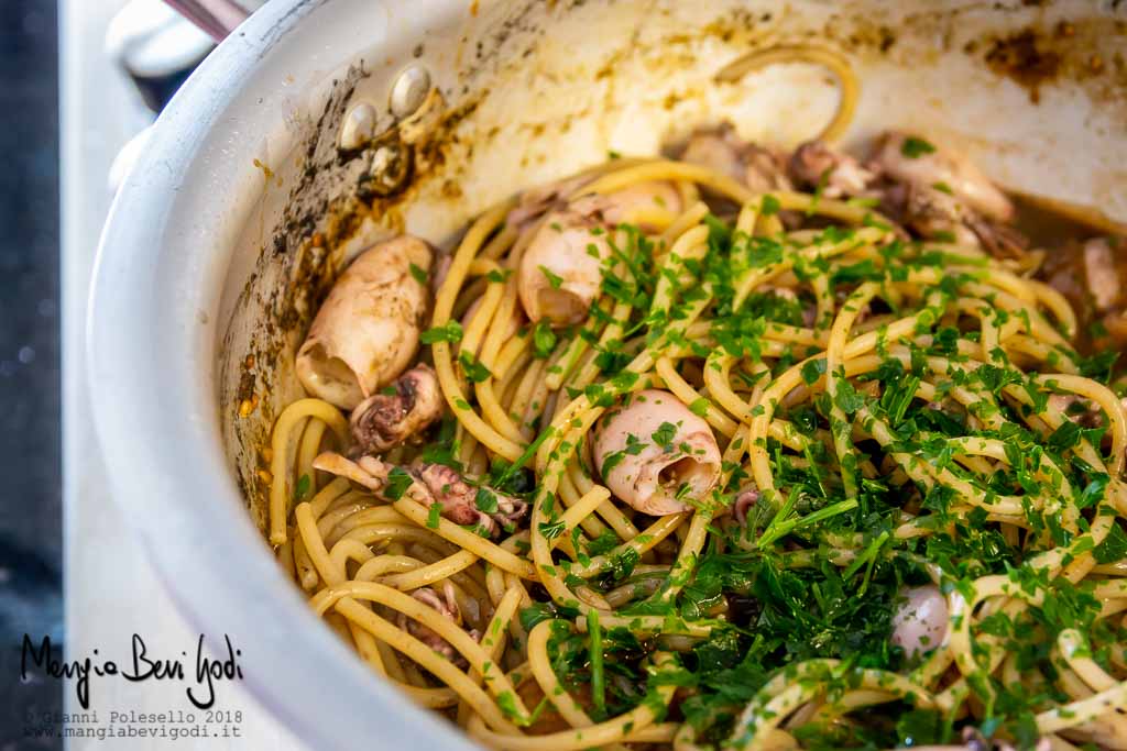 Saltare gli spaghetti con calamaretti in padella e aggiungere prezzemolo tritato
