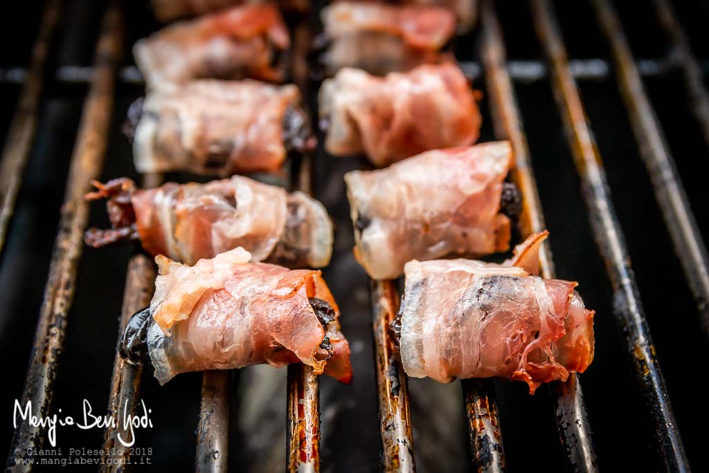 Involtini di prugne e pancetta in cottura sulla griglia del barbecue