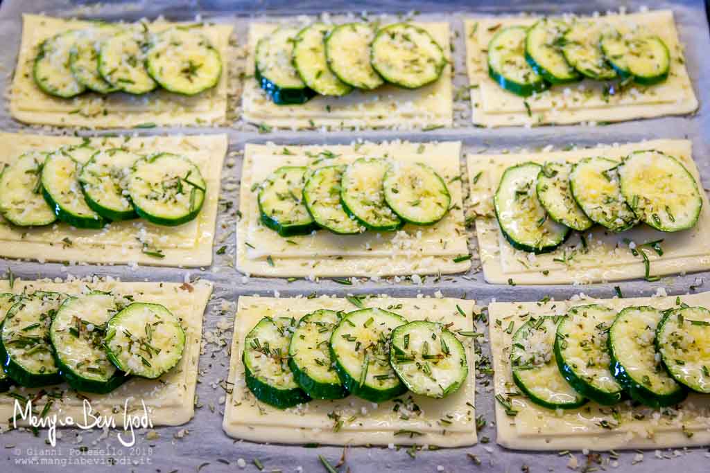 Preparazione rettangoli di pasta sfoglia con zucchine, rosmarino e formaggio.