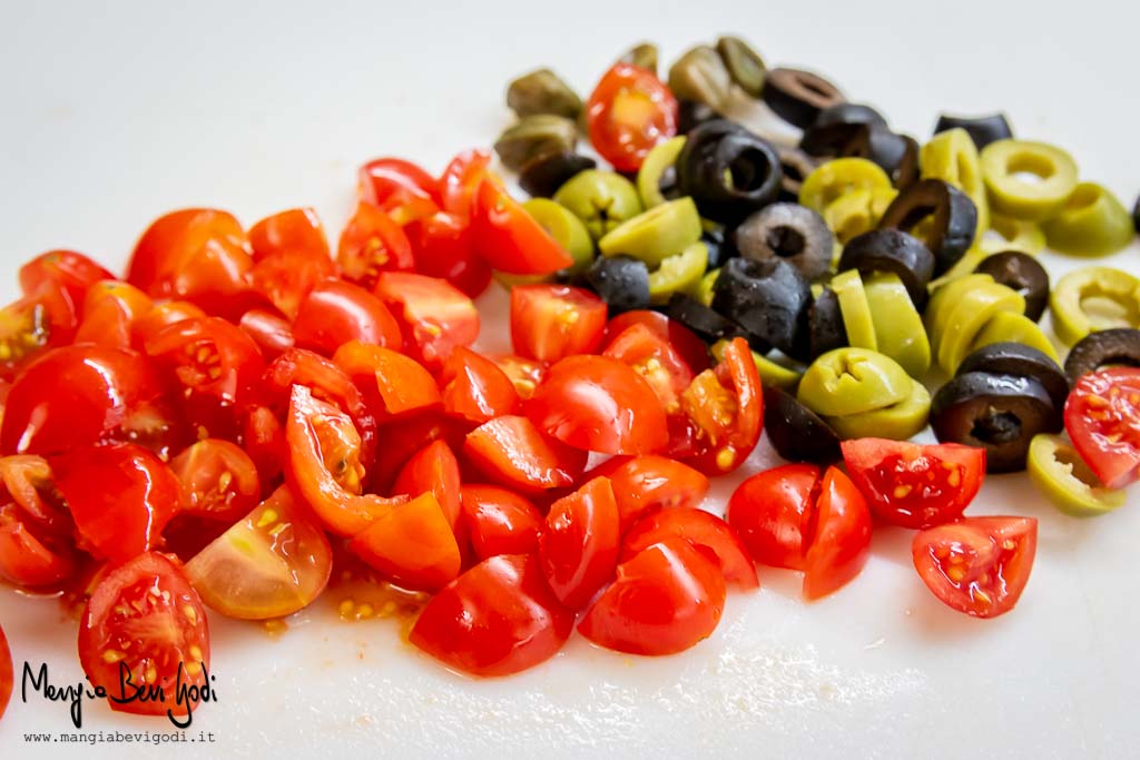 Tagliare i pomodorini, i capperi e le olive