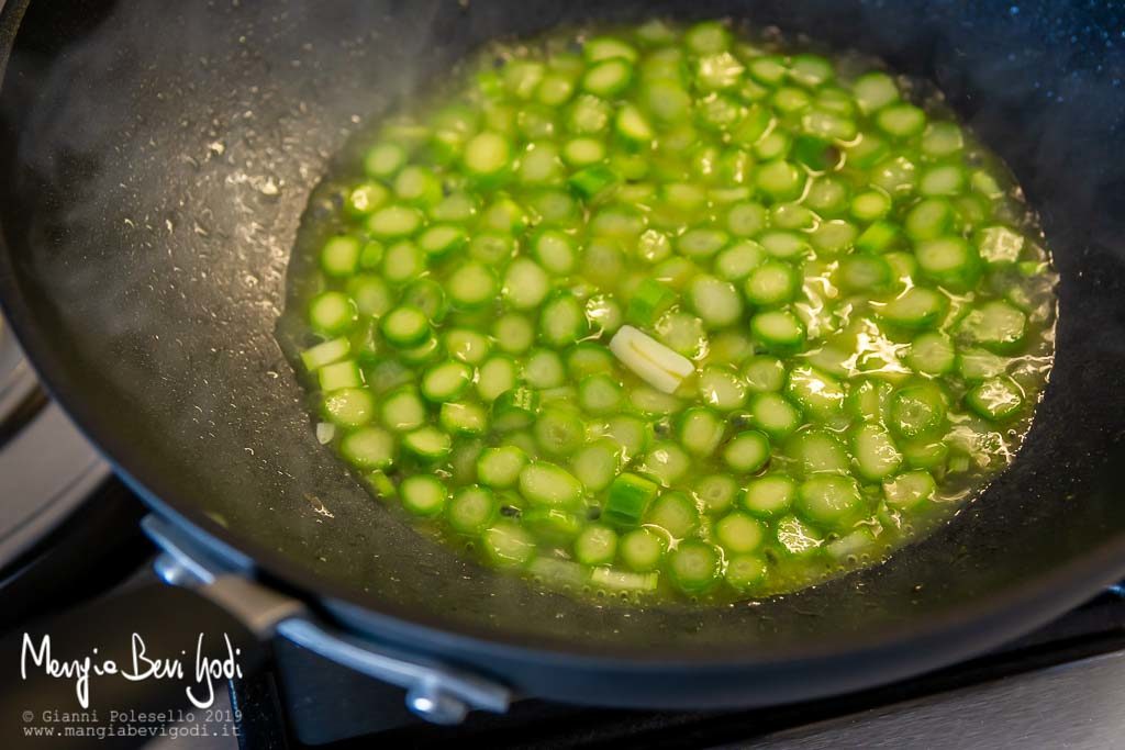 Gambi di asparagi tagliati a rondelle in cottura dentro un wok antiaderente