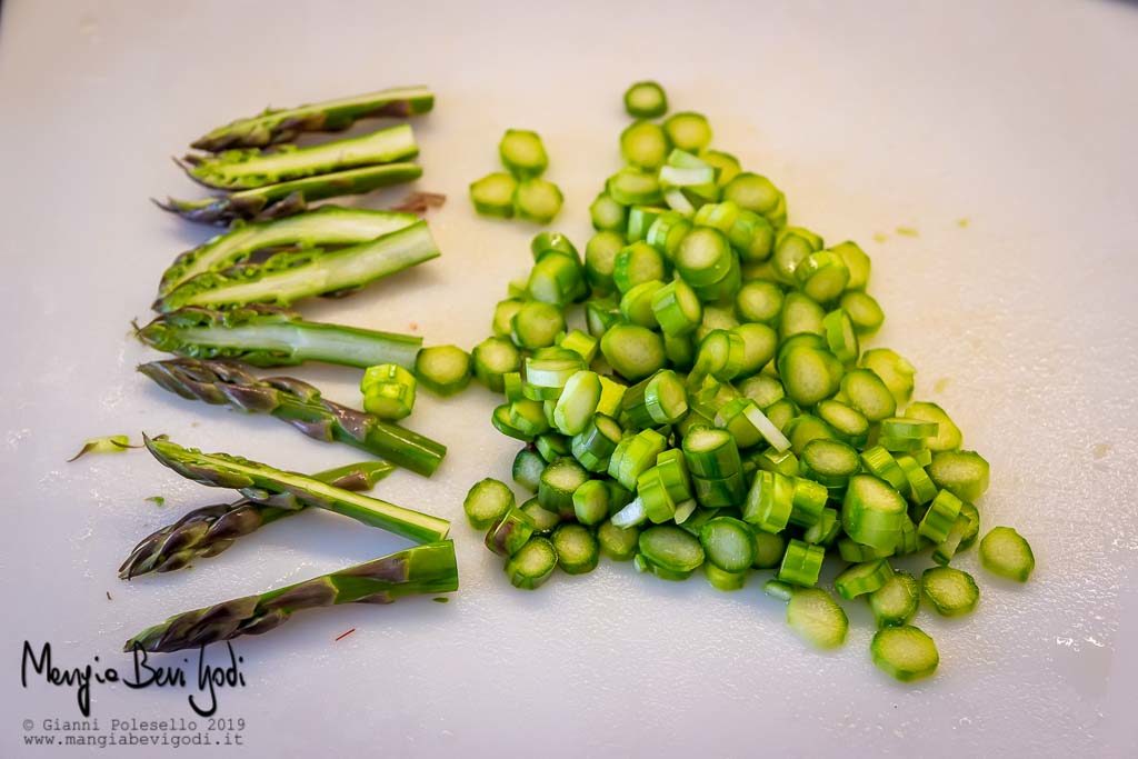 Asparagi verdi su tagliere bianco. Le punte sono tagliate a metà per lungo mentre i gambi sono tagliati a rondelle sottilissime