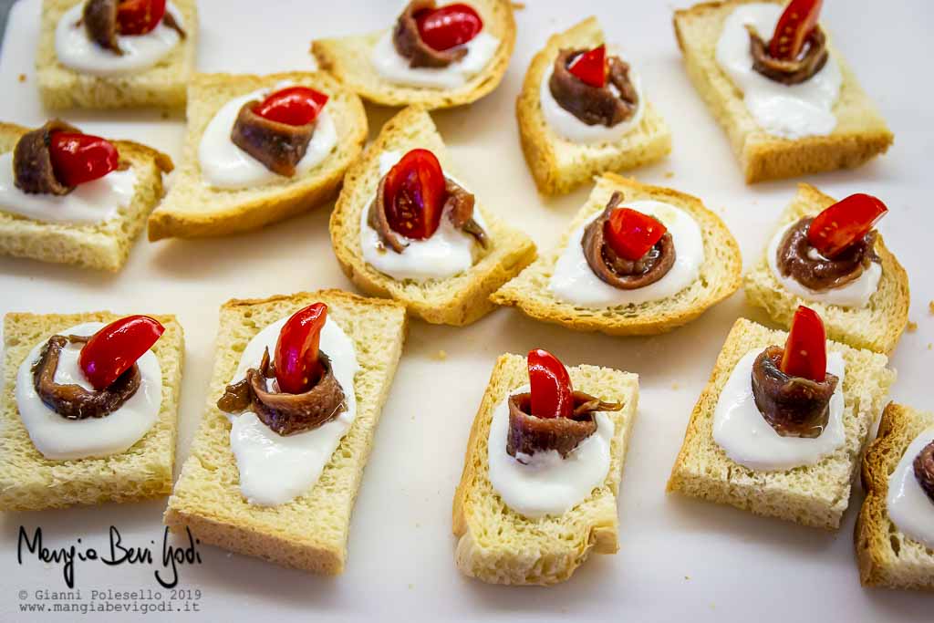 Crostini con burrata, alici e pomodorini su tagliere bianco