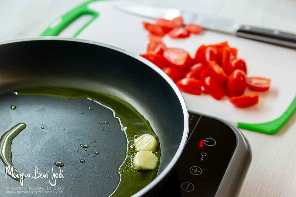 Soffritto di aglio in padella e tagliere con pomodorini