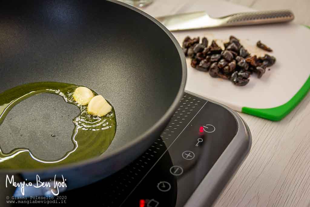 Soffritto di aglio in padella e tagliere con olive nere