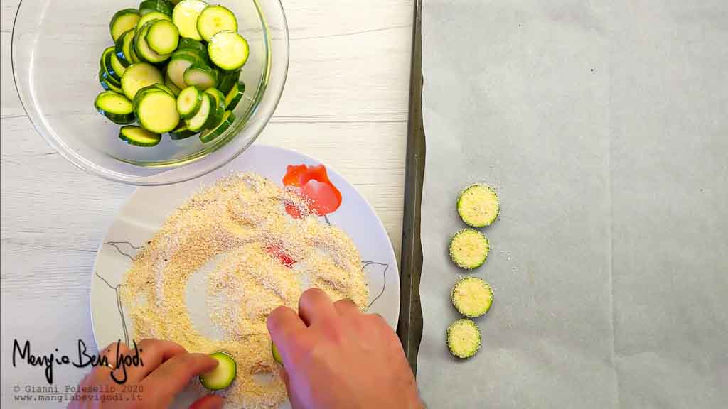 Distribuire la panatura al parmigiano sulle chips di zucchine